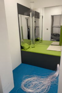 Sensory room B:  This is a photo of a sensory room in LOETB, There is a green padded plinth surrounding a large bubble tube. Behind the plinth is two wall mounted mirrors. 